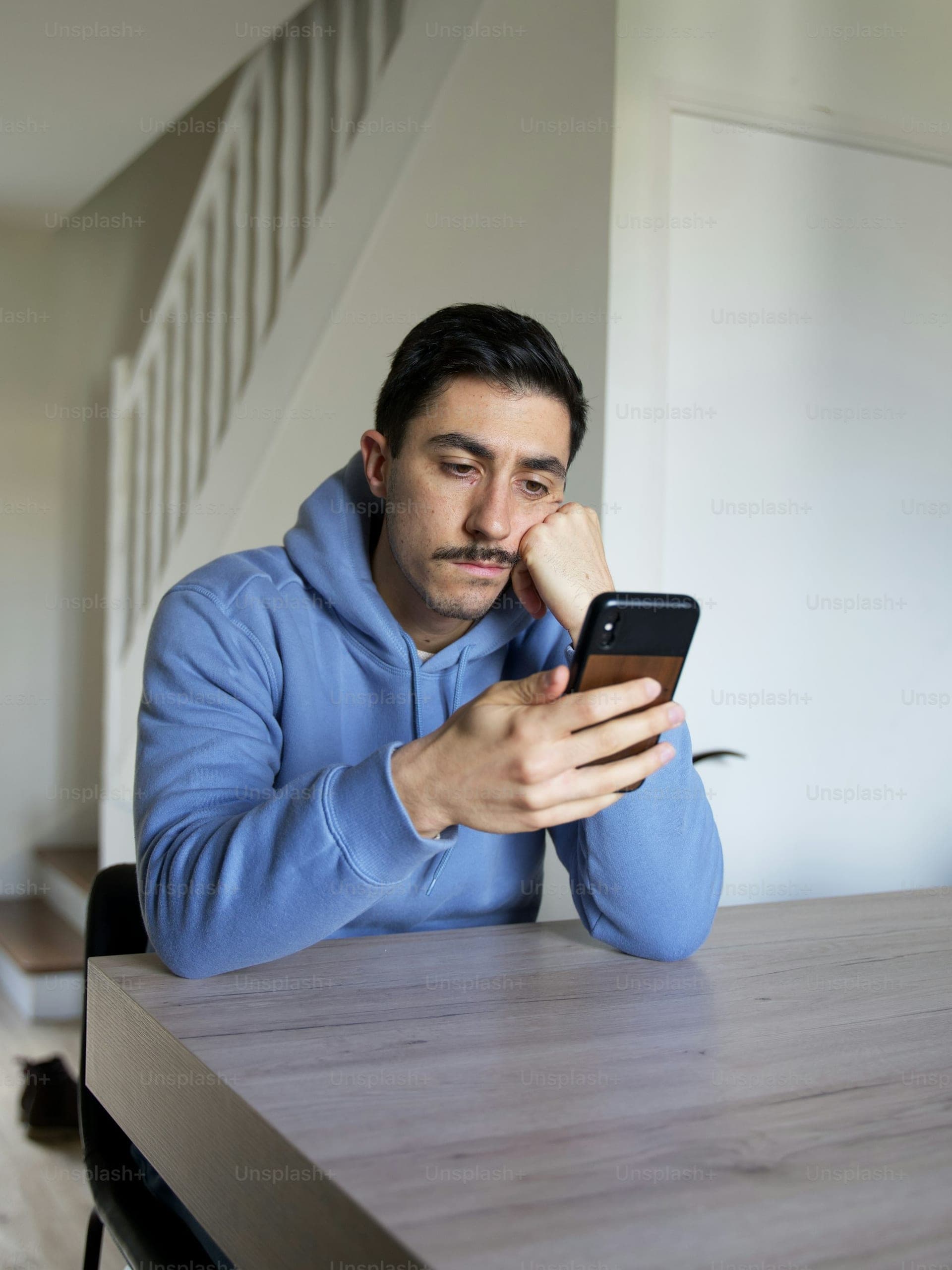 A young man at a table, looking at his phone