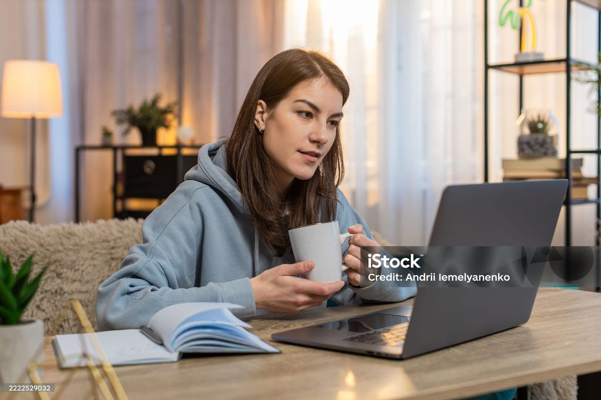 A young woman with a mug of coffee, reading at her laptop at home